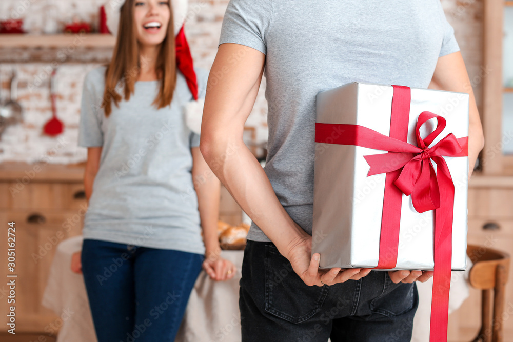 Happy young man giving Christmas present to his girlfriend at home