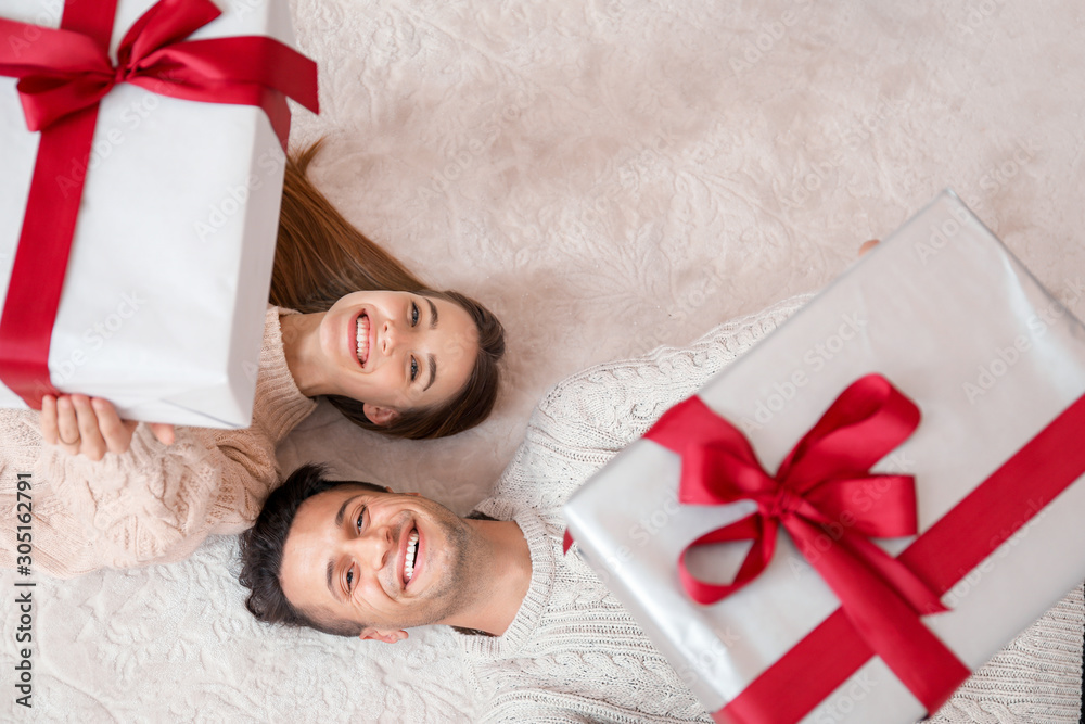 Happy young couple with Christmas gifts lying on floor, top view