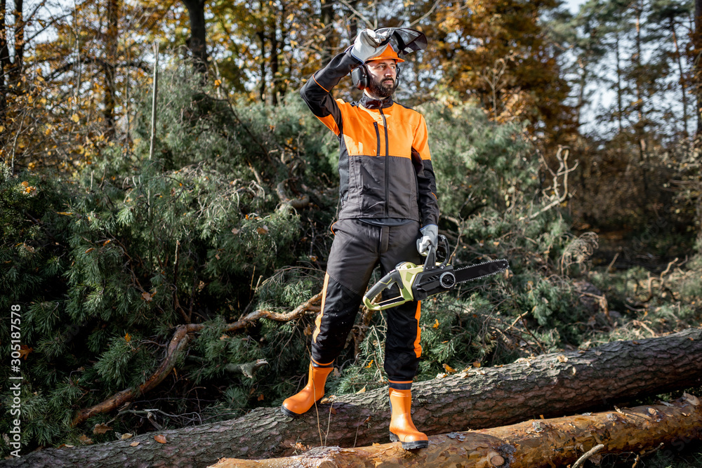 Full length portrait of a professional lumberjack in protective workwear standing with a chainsaw on