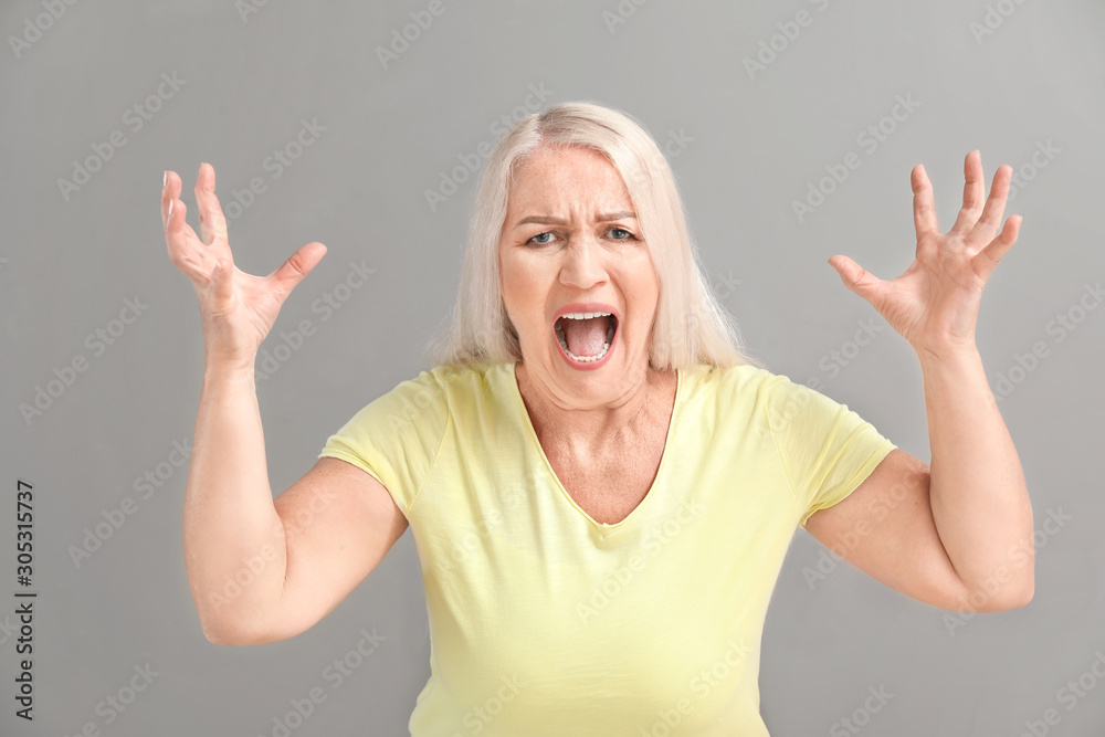 Angry mature woman on grey background