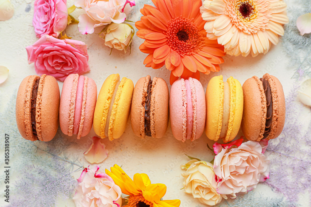 Different tasty macarons with flowers on white background