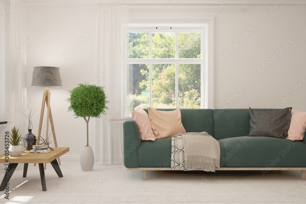 Stylish room in white color with sofa and summer landscape in window. Scandinavian interior design. 