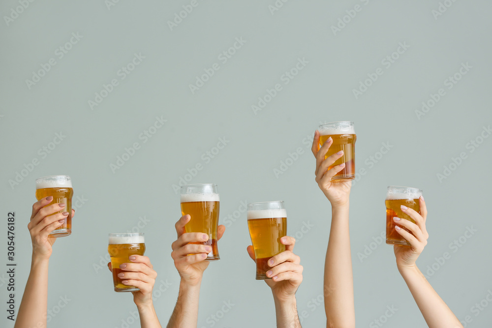 Hands with glasses of beer on grey background