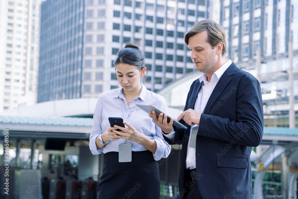 Business man holds Laptop and discusses work with female  technician.Theyre Standing at a building 