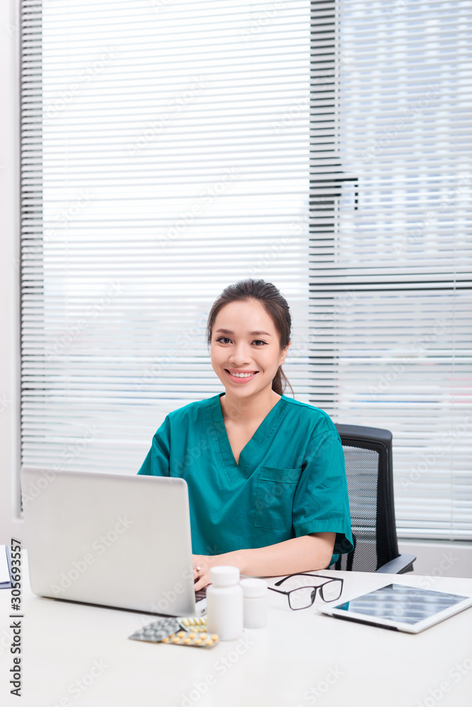 Female doctor working at office desk and smiling at camera, office interior