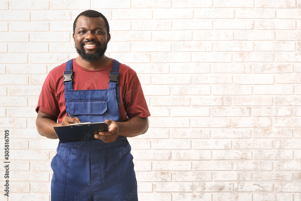 African-American car mechanic with clipboard near brick wall