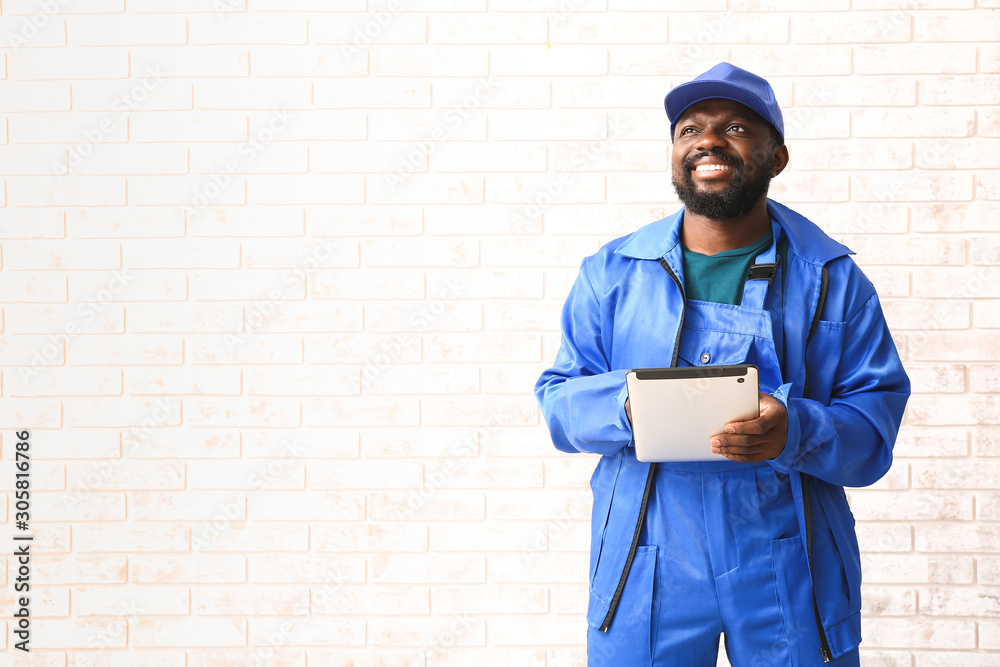 African-American car mechanic with tablet computer near brick wall