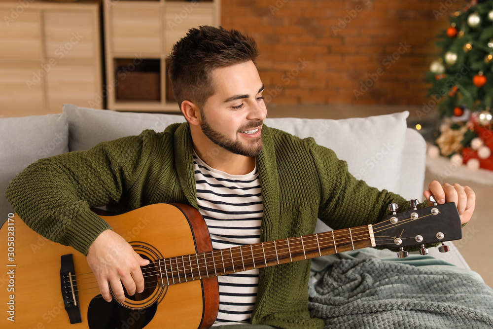 Handsome young man playing guitar at home on Christmas eve