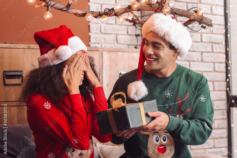 Happy African-American man giving Christmas present to his wife at home