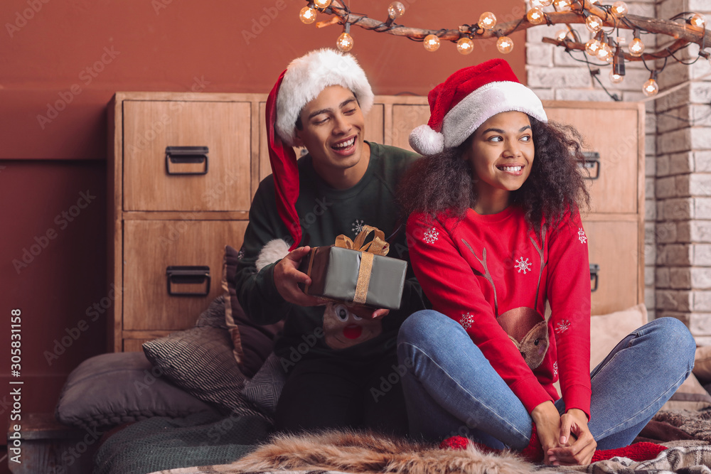 Happy African-American man giving Christmas present to his wife at home