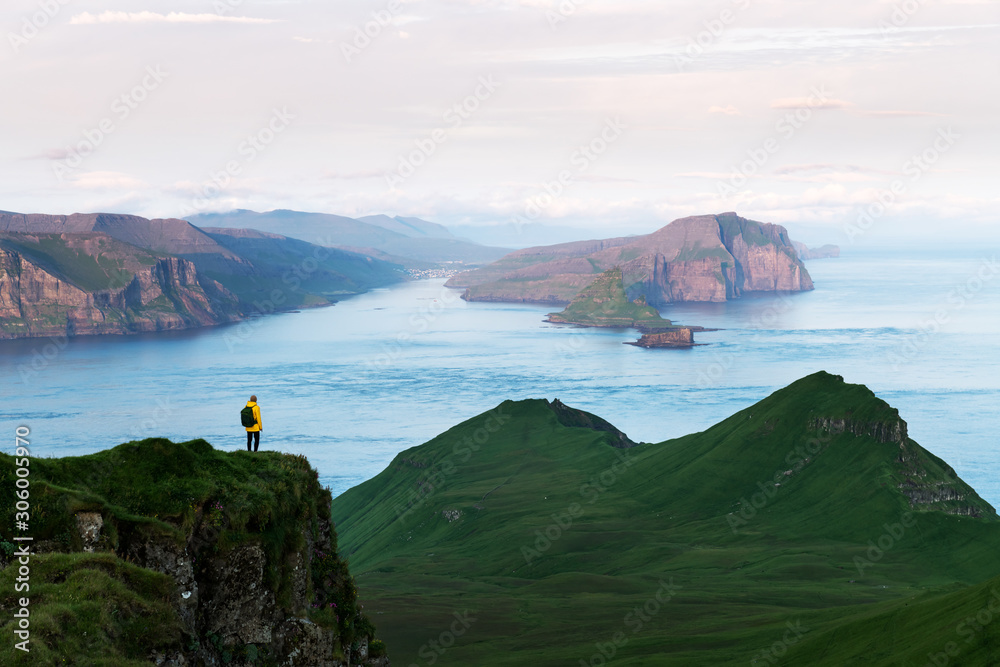 Lonely tourist in yellow jacket looking over majestic Alaberg cliffs on Mykines island, Faroe Island