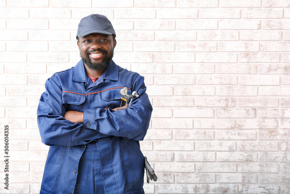 African-American car mechanic near brick wall