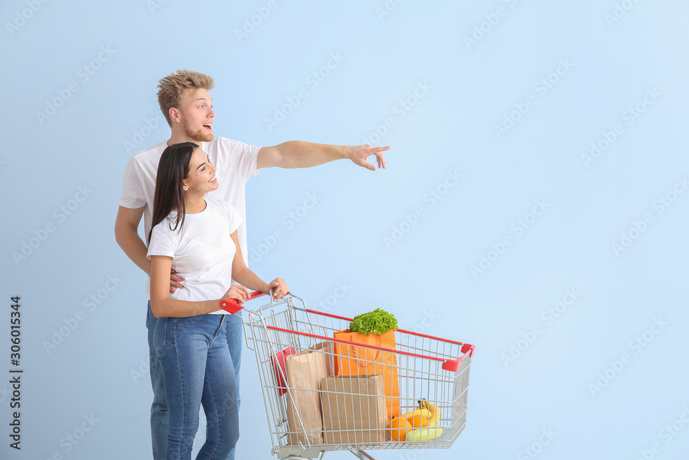 Couple with shopping cart on color background