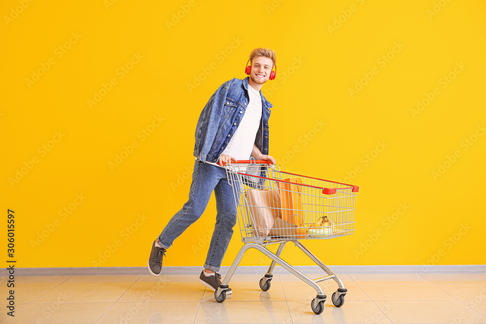 Young man with shopping cart near color wall