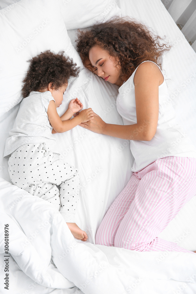 Little African-American girl with mother sleeping in bed