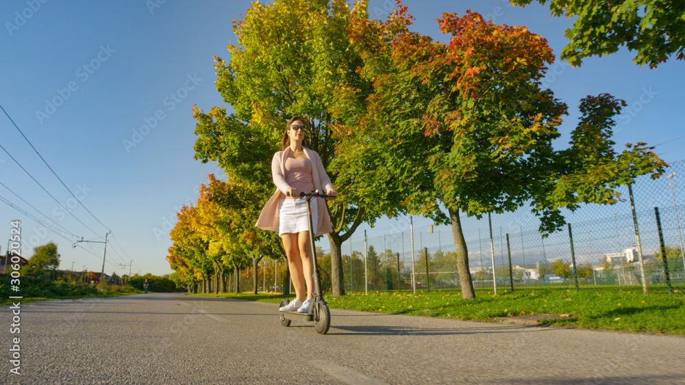 LOW ANGLE: Young woman cruises along the autumn colored road on sunny afternoon.