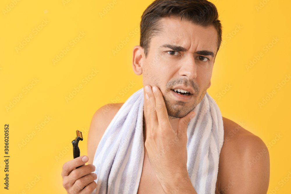 Displeased young man with razor on color background