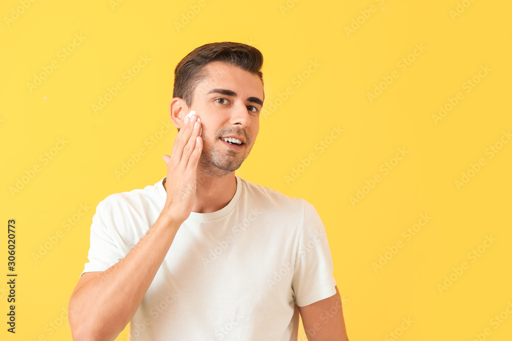 Handsome young man applying shaving foam against color background