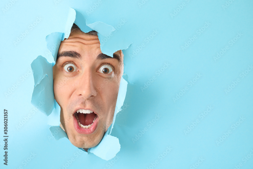 Shocked shaved young man looking out of hole in color paper