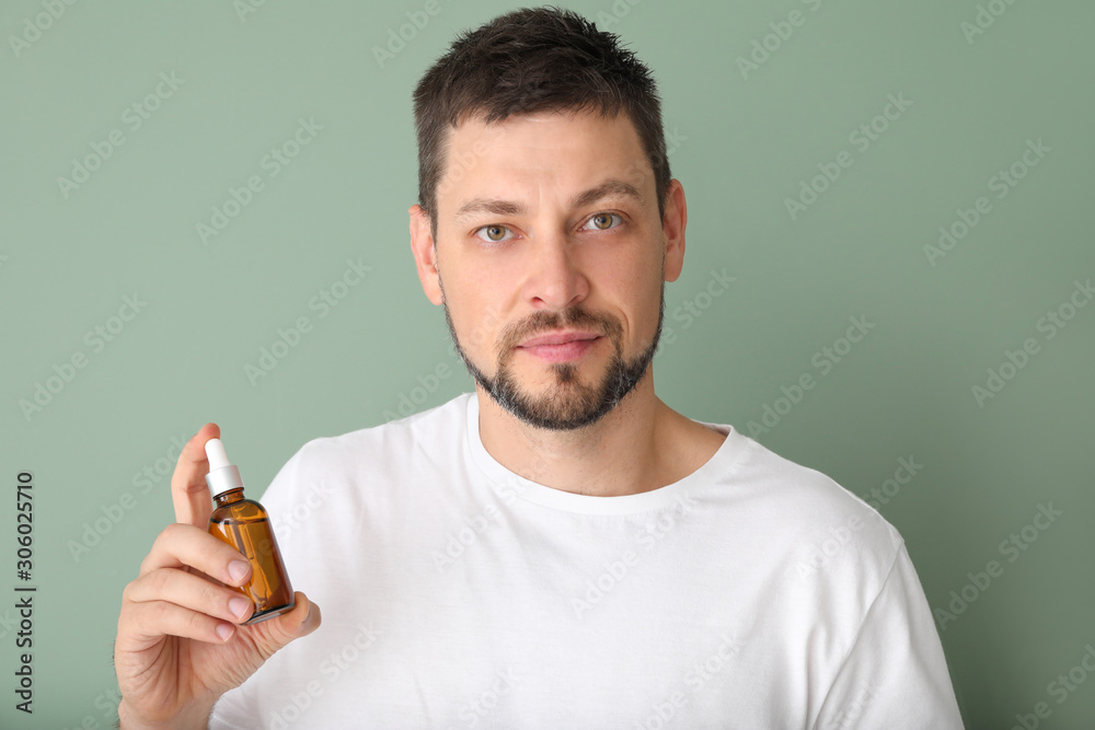 Handsome man with cosmetic product on color background