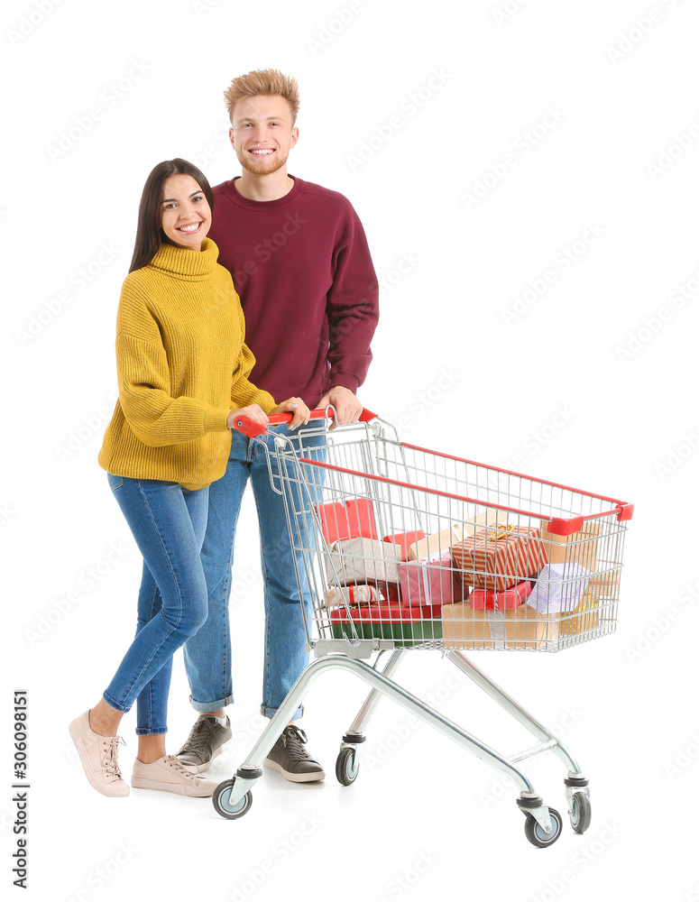 Young couple with shopping cart full of Christmas gifts on white background