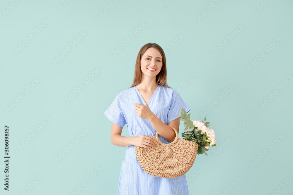 Beautiful young woman with bag and bouquet of carnation flowers on color background