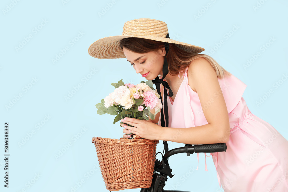 Beautiful young woman with bicycle and bouquet of carnation flowers on color background