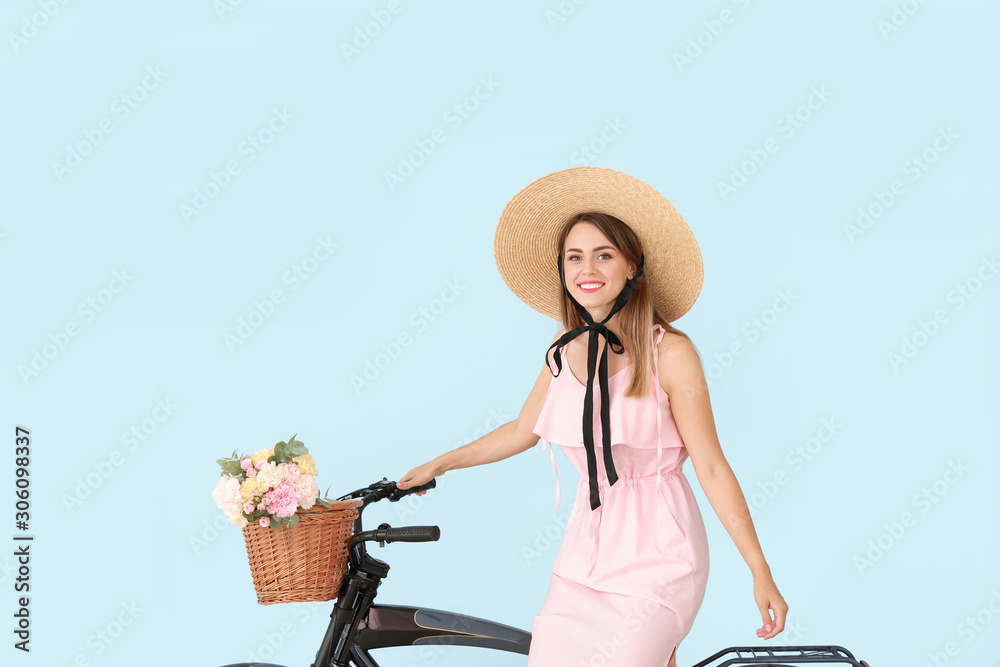 Beautiful young woman with bicycle and bouquet of carnation flowers on color background