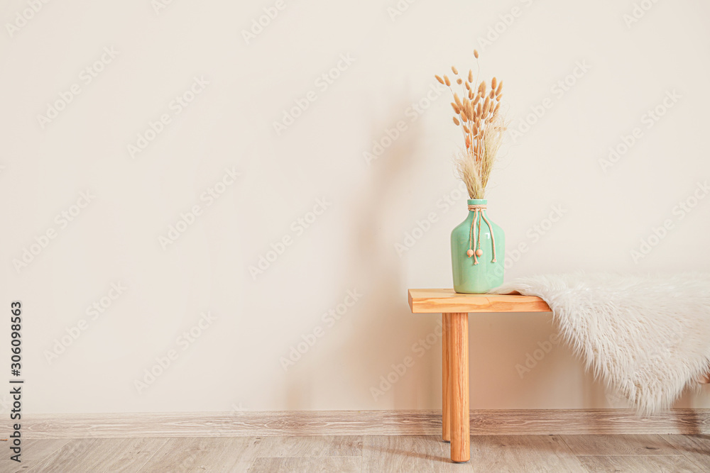 Wooden table with vase and plaid near white wall