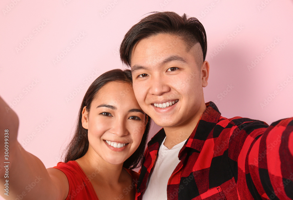 Portrait of happy young Asian couple taking selfie on color background