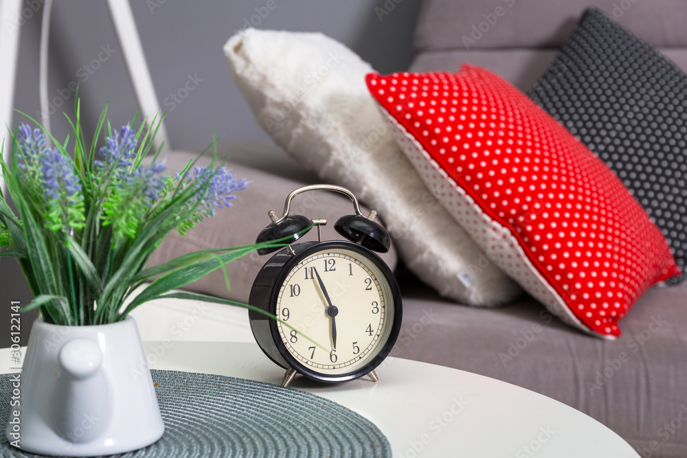 Analog alarm clock on the table in bedroom with colorful pillows