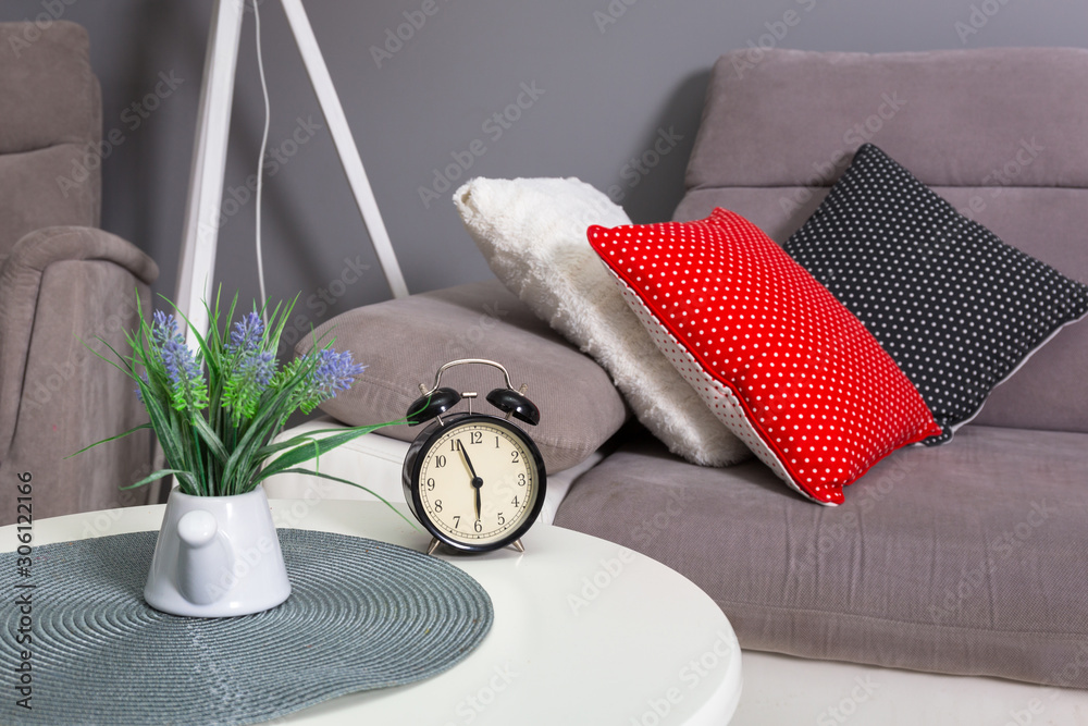 Analog alarm clock on the table in bedroom with colorful pillows