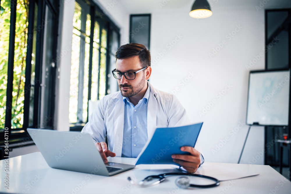 Portrait of handsome doctor working with laptop and documents.