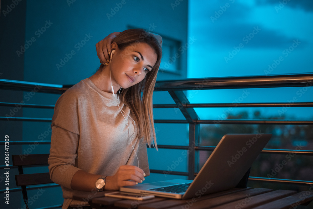 Young woman with earphones using laptop at night.