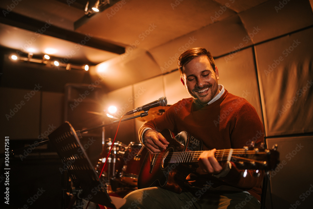 Smiling man playing guitar in recording studio, portrait, copy space.