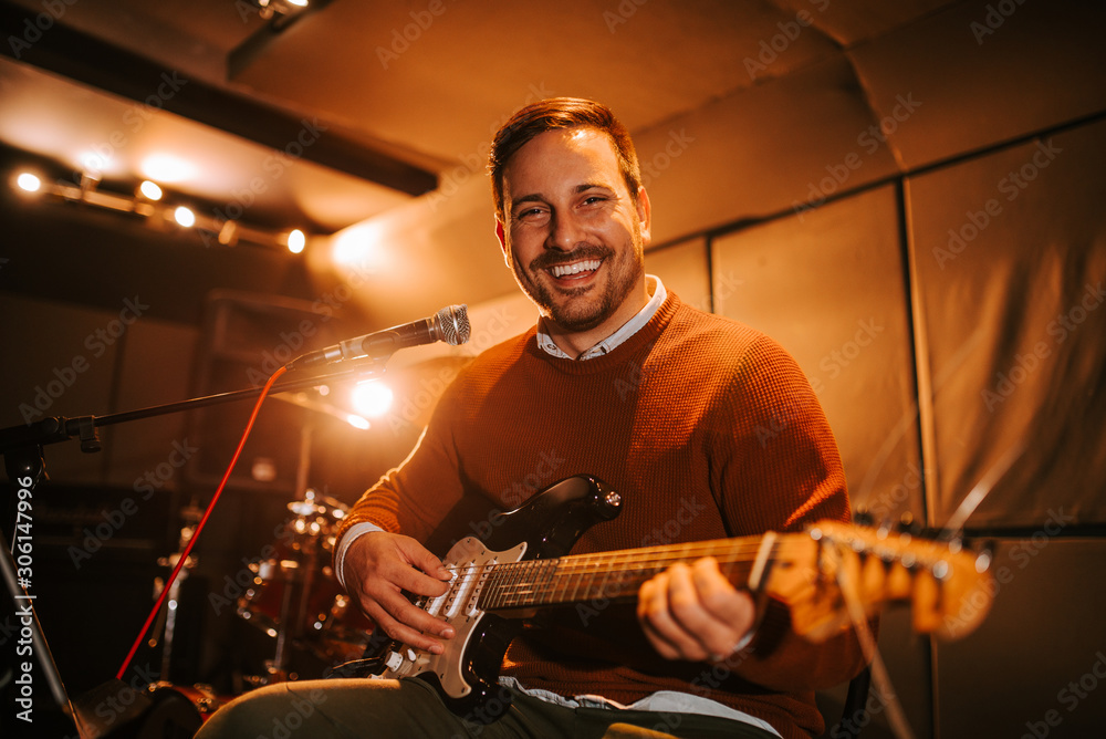 Portrait of a guitarist playing on stage, looking at camera.