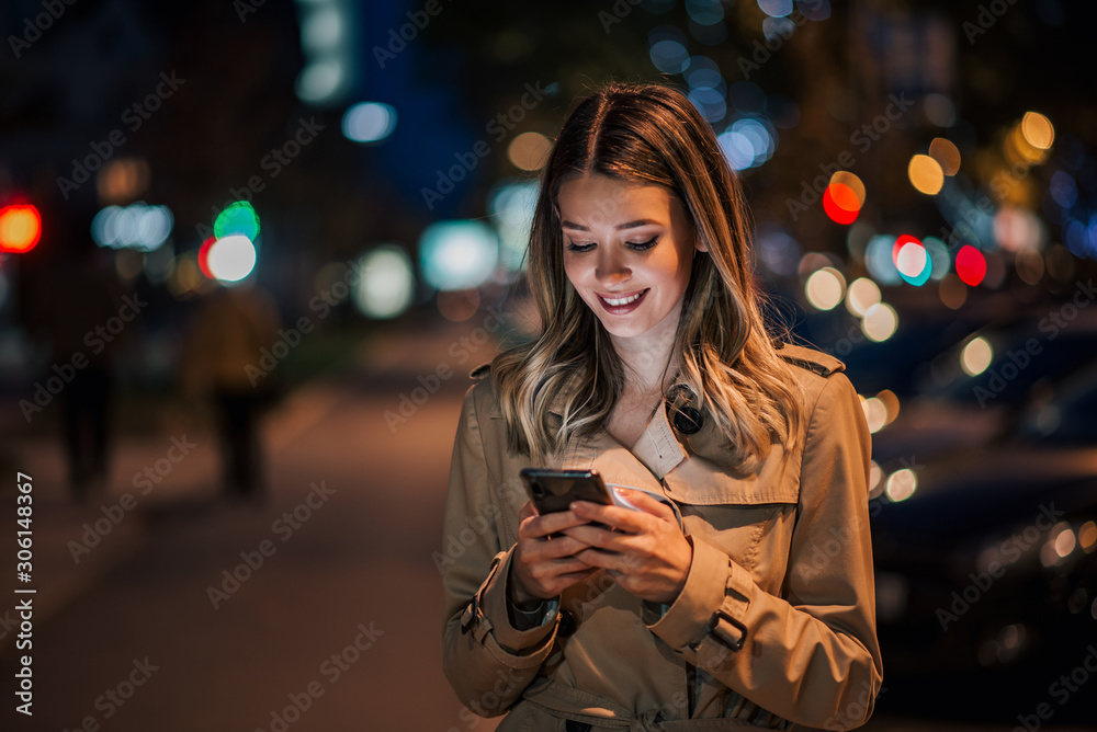 Portrait of a smiling young woman using smart phone at night.