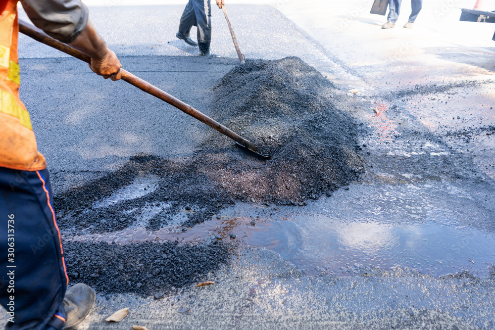 道路工人在道路上使用铲子擦拭沥青进行工作。