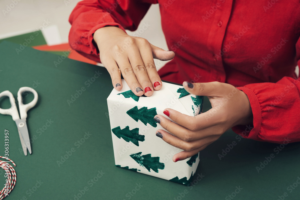 Female hands wrap christmas gift on blue background close up. Xmas concept, noel decorations.