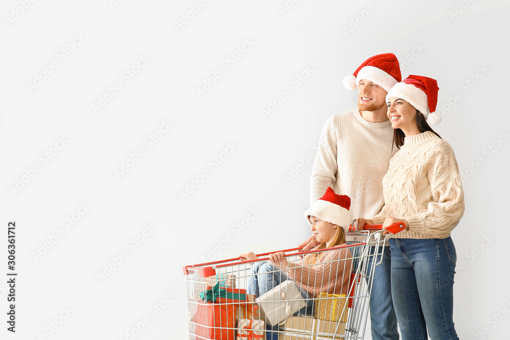 Family with shopping cart full of Christmas gifts on light background