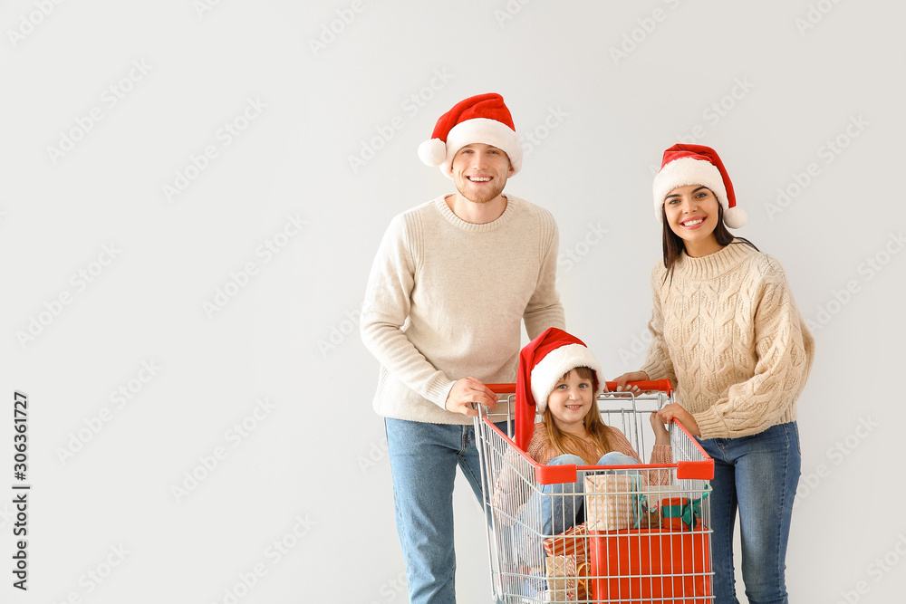 Family with shopping cart full of Christmas gifts on light background