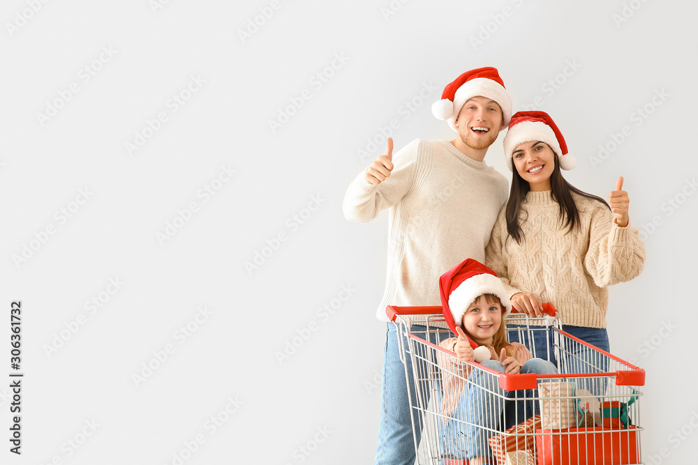 Family with shopping cart full of Christmas gifts showing thumb-up on light background