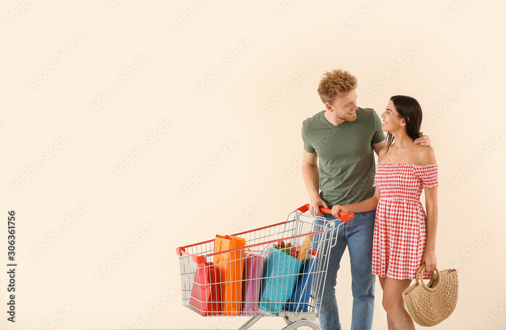 Young couple with shopping cart on light background