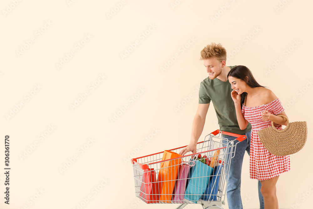 Young couple with shopping cart on light background