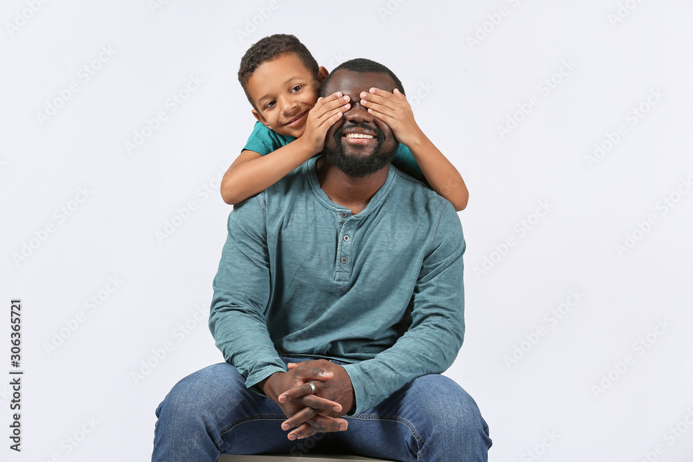 Portrait of African-American man with his little son on light background