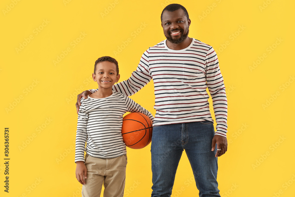 Portrait of African-American man and his little son with ball on color background