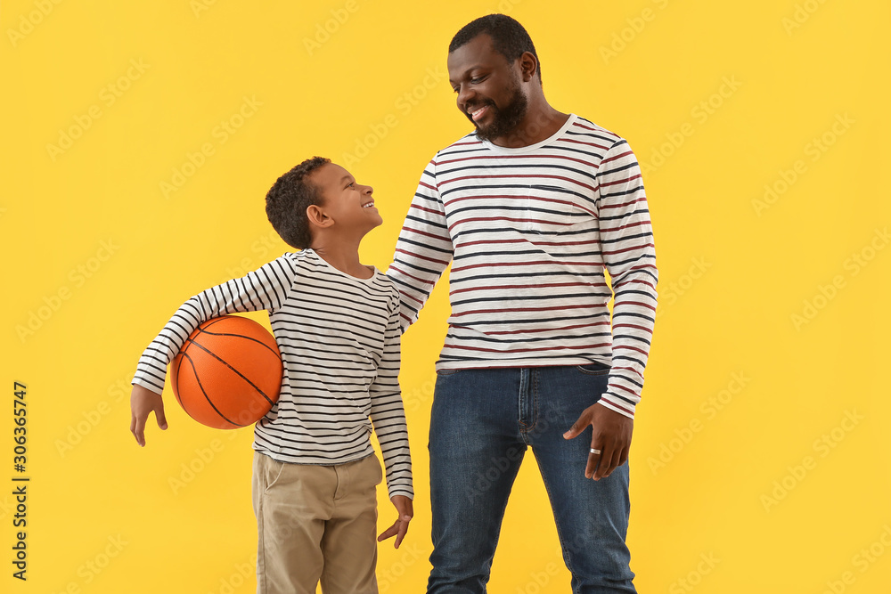 Portrait of African-American man and his little son with ball on color background