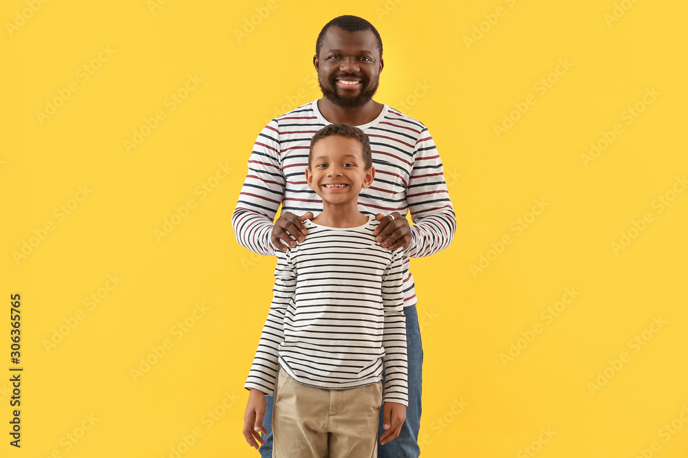 Portrait of African-American man with his little son on color background