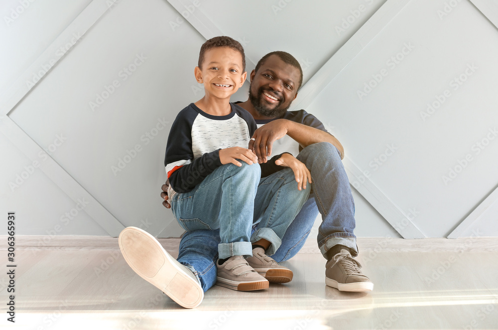 Portrait of African-American man with his little son sitting near light wall