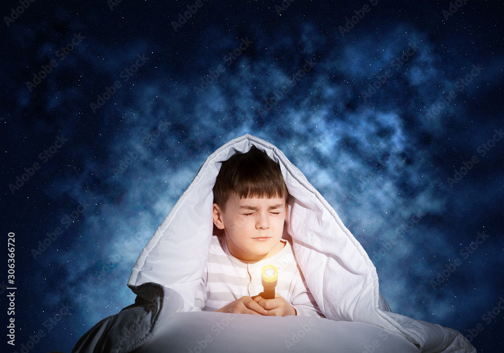 Frightened child with flashlight under blanket